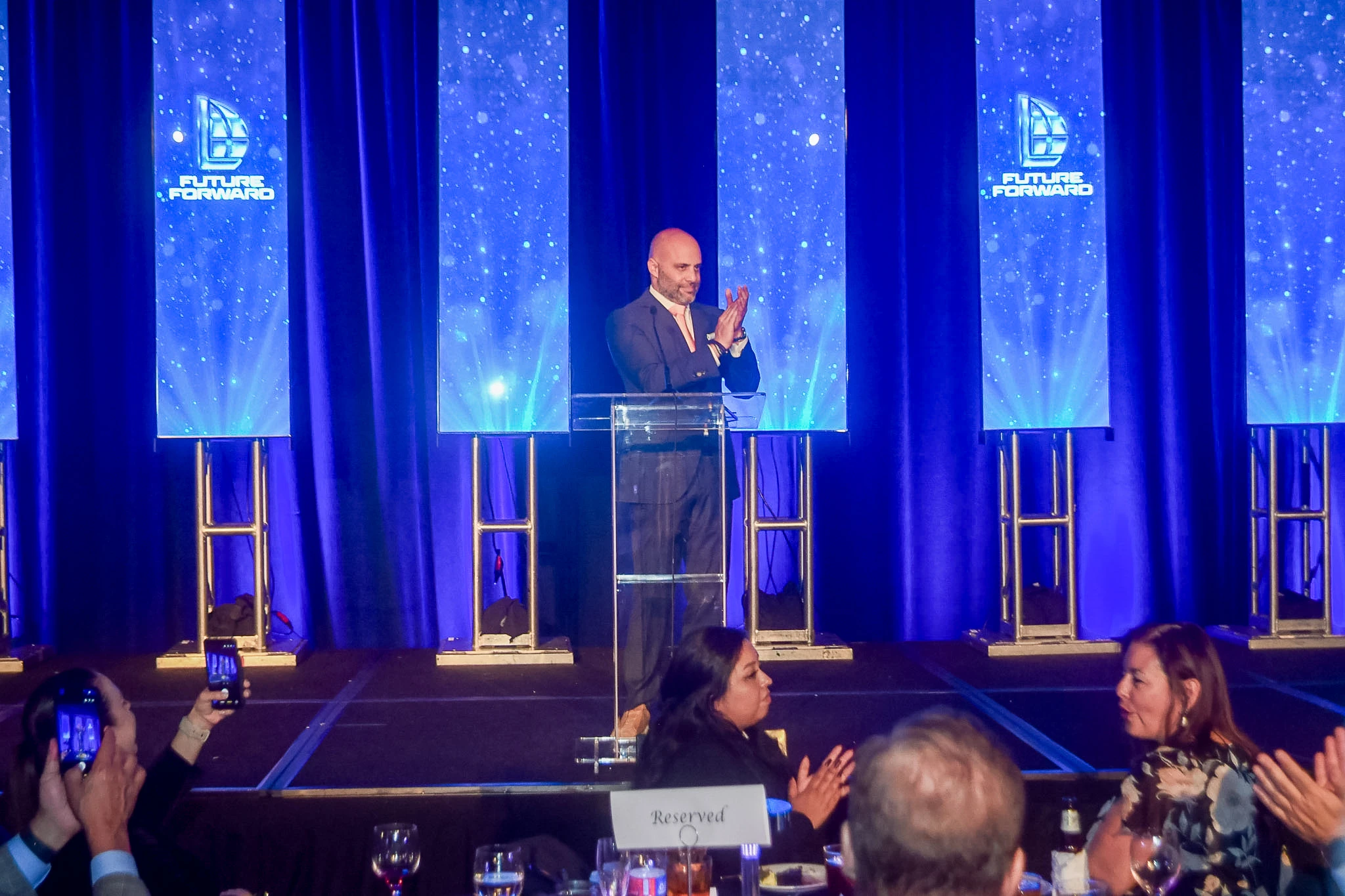 A speaker applauding on the illuminated LYND conference stage
